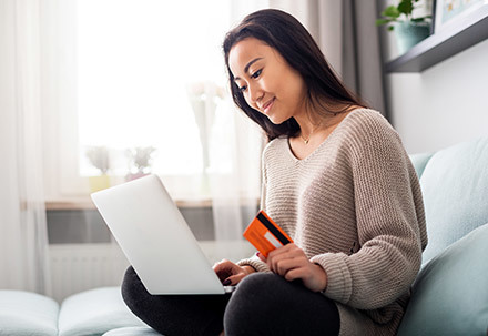 Retail campaign image showing a woman on her sofa with a credit card and her laptop